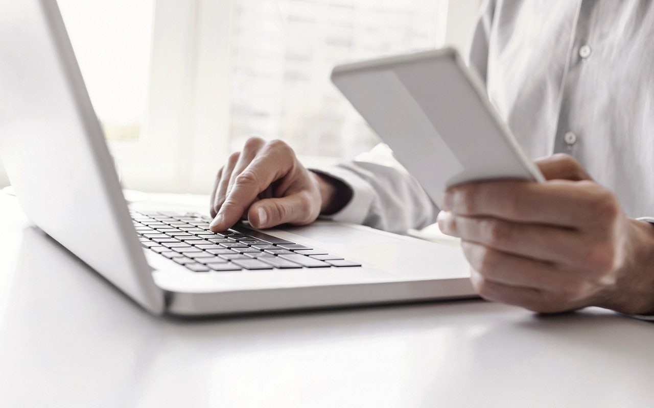 mann arbeitet am laptop und hält dokument in der hand